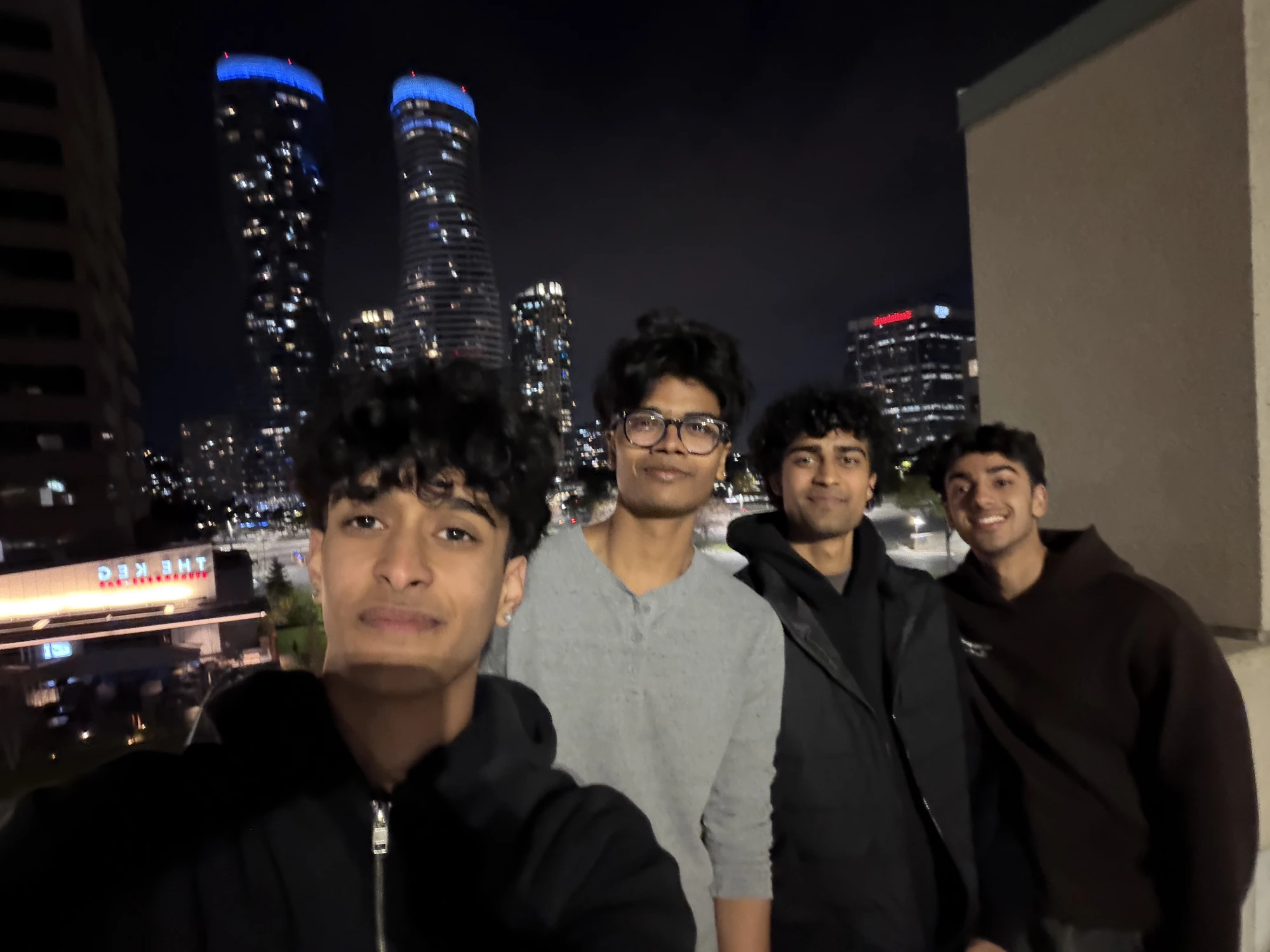Dev and friends in front of a city skyline at night
